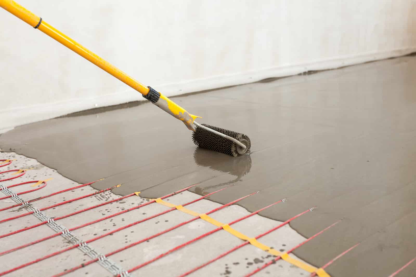 Electric floor heating system installation in new house. Worker align cement with roller